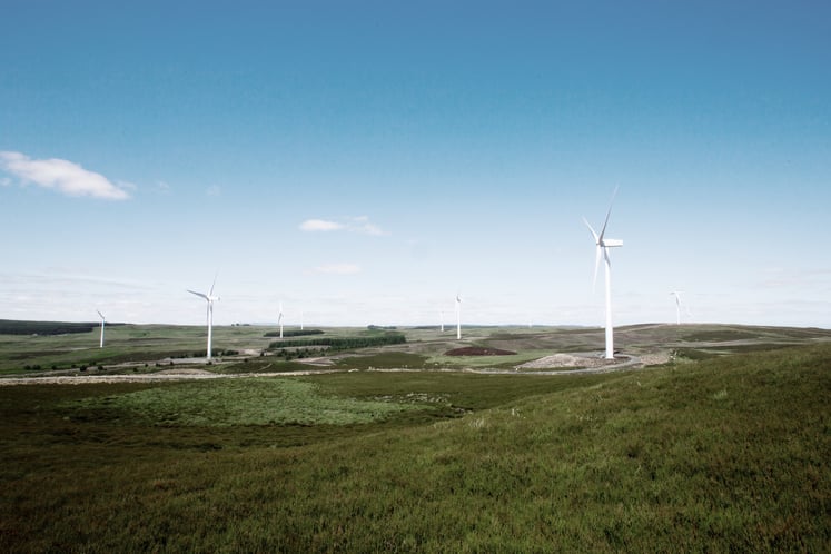 Photo of wind turbines located in a green landscape, with blue skies above.